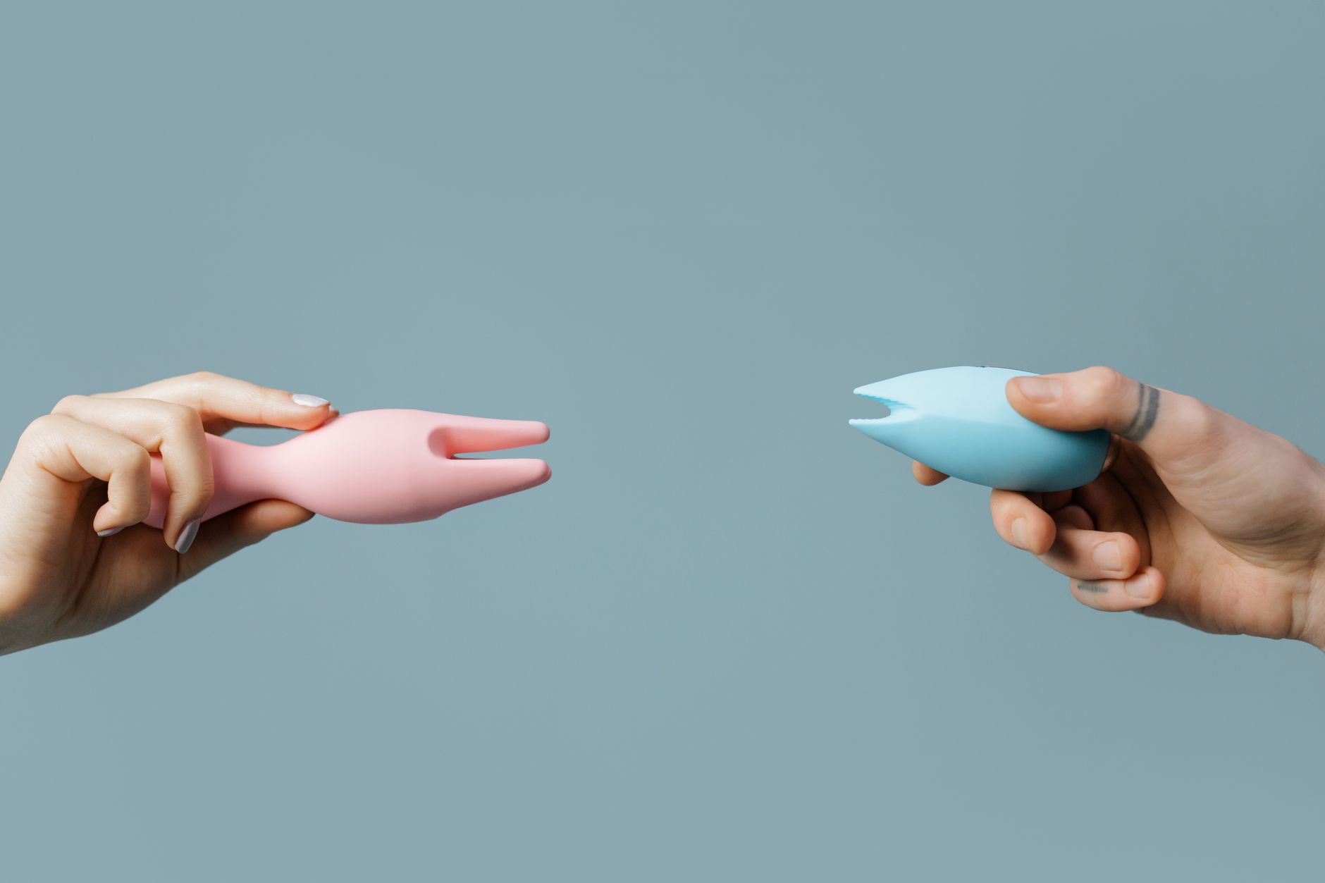 Woman holding blue and pink silicone vibrators in a contemplative manner against soft background.